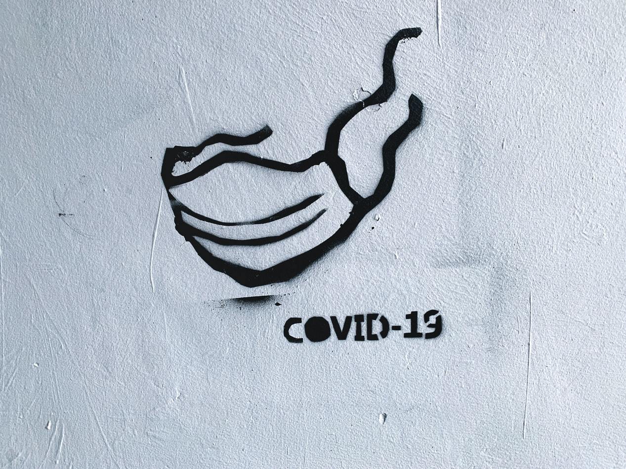 Black graffiti on a white wall representing a facial mask, with the words 