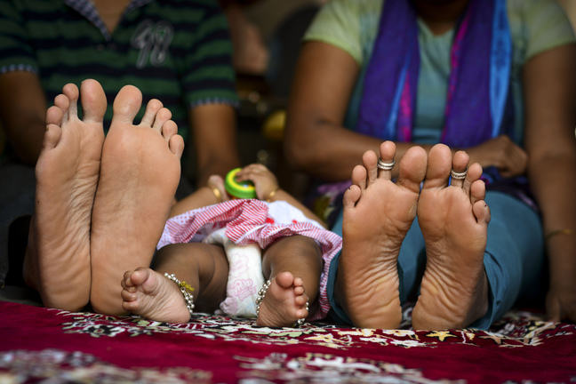 Image of a baby's feet in the middle of two adults' feet.
