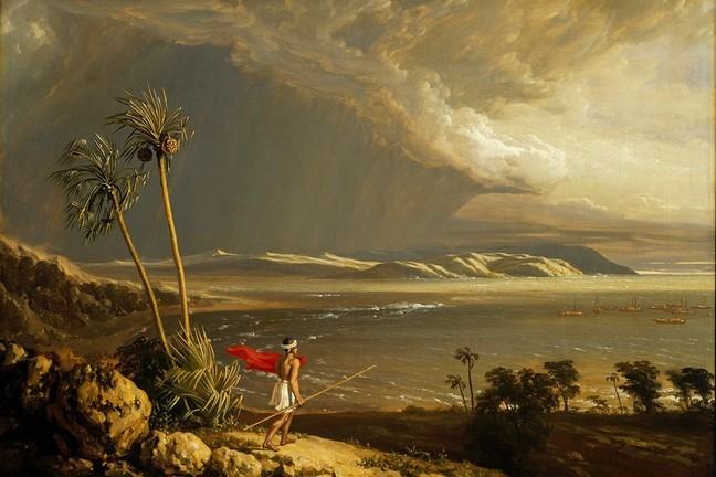 Indigenous figure with red cloak and spear, stands looking across a bay with palm trees and dramatic skyline. Boats are in the bay in the distance.
