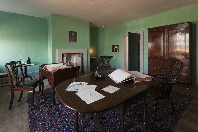 A photograph of a wooden table and desk with wooden chairs