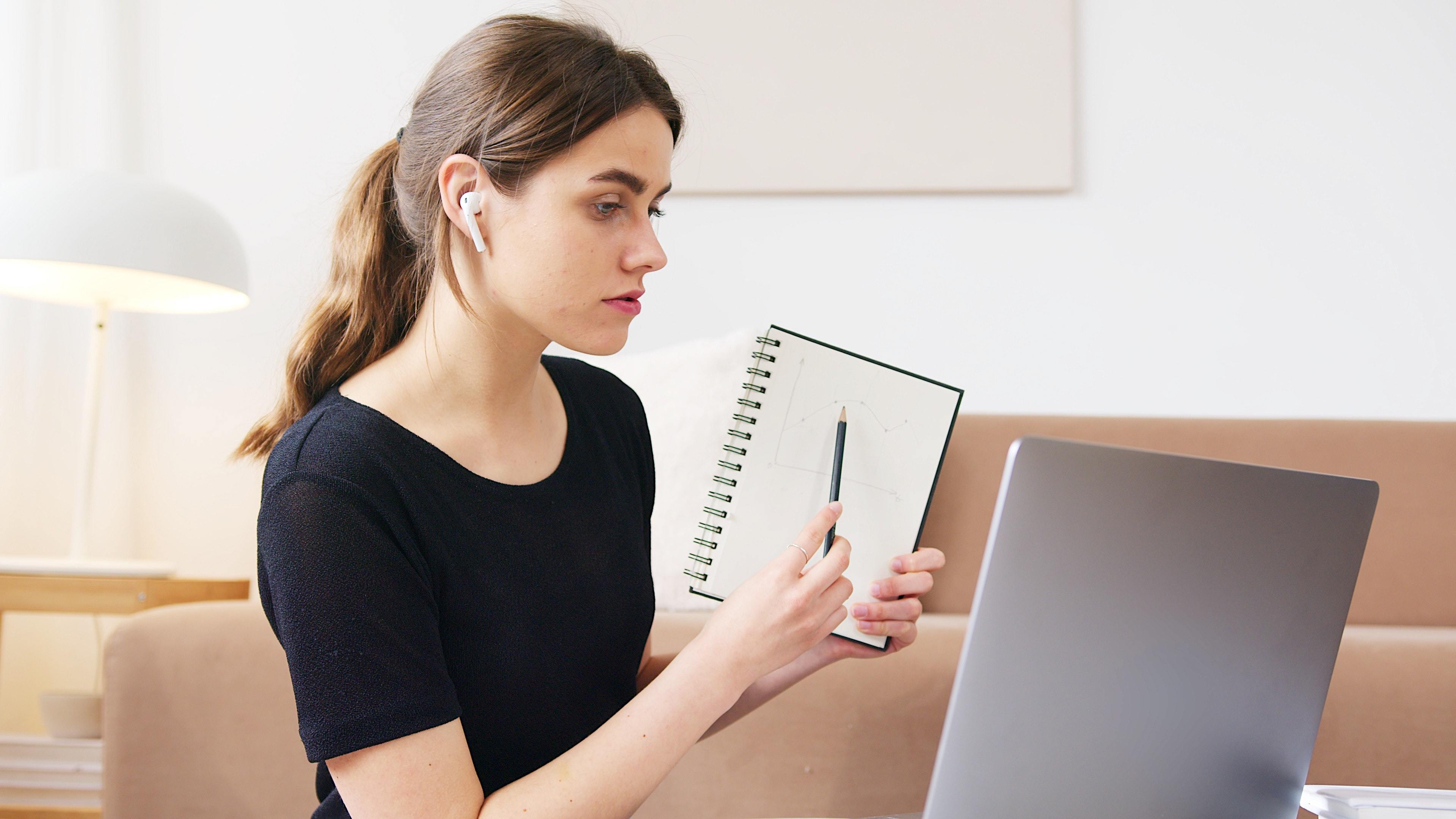 Lady pointing at a pad of paper, filming on her webcam