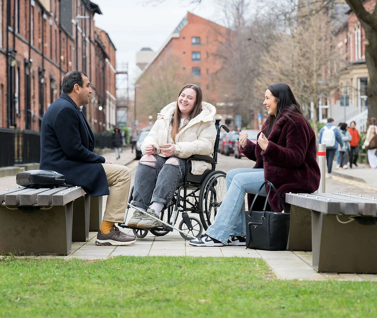 Visually impaired man chatting with a lady in a wheelchair and another lady in an open space.