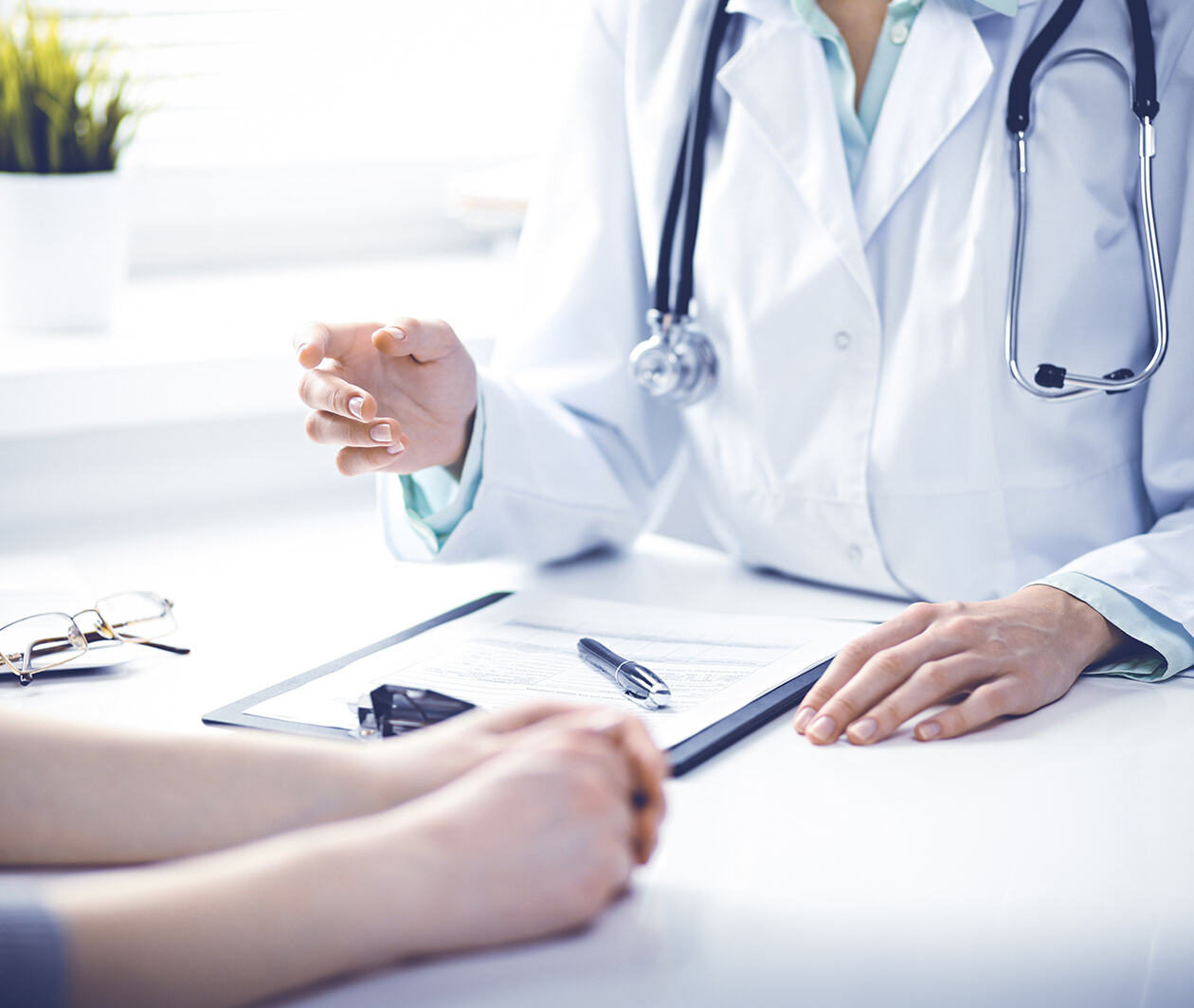 Doctor and female patient sitting at the desk and talking in clinic near window. Medicine and health care concept. Green is main color A