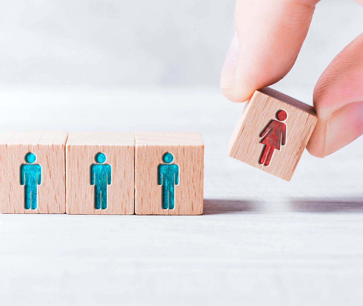 Male Fingers Adding A Block With A Different Colored Female Icon To 3 Blocks With Equal Colored Man Icons On A Table