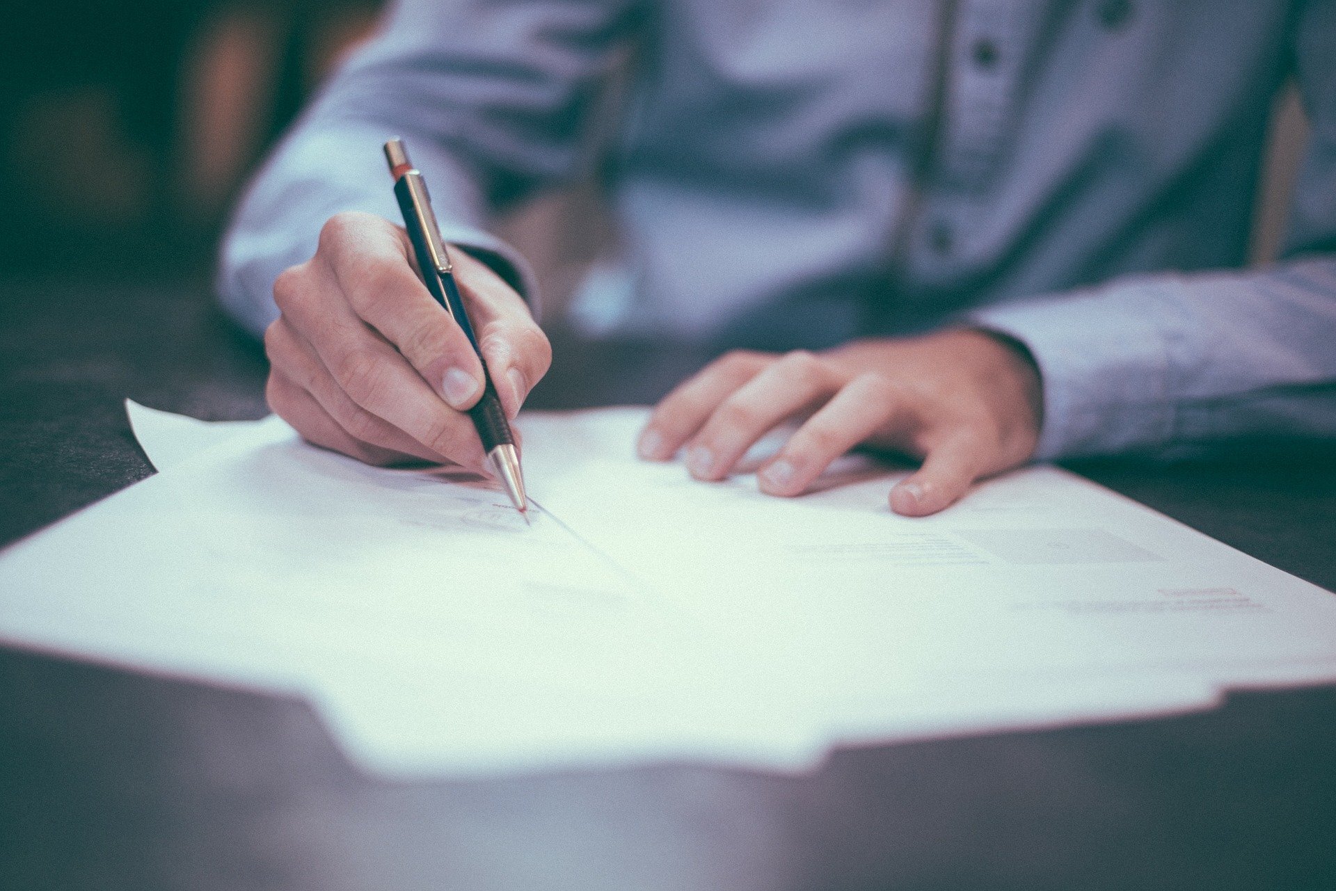 Man writing with a pen on a small pile of three sheets of A4 paper