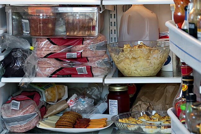 An open refrigerator door showing a full stocked fridge loaded up with food and fresh ingredients