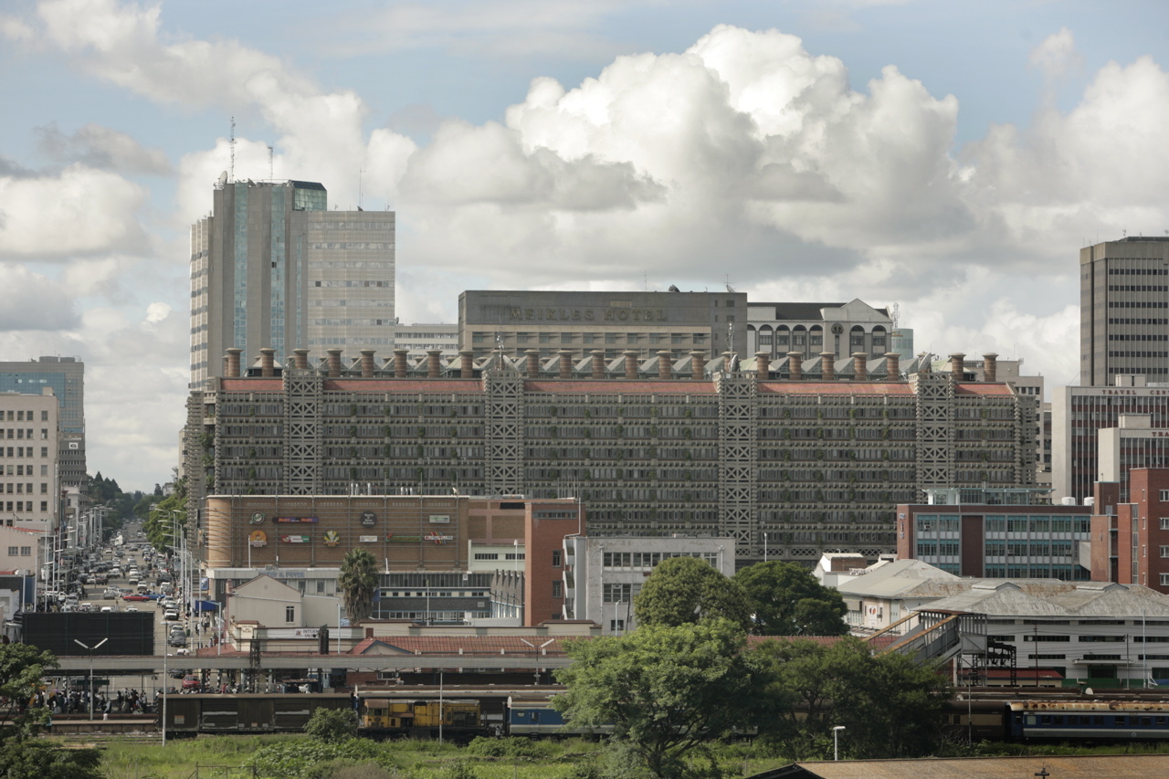 An image of the The pink-hued Eastgate Centre, in Harare Zimbabwe, with its distinctive chimneys and pink hued facade, surrounded by other buildings.