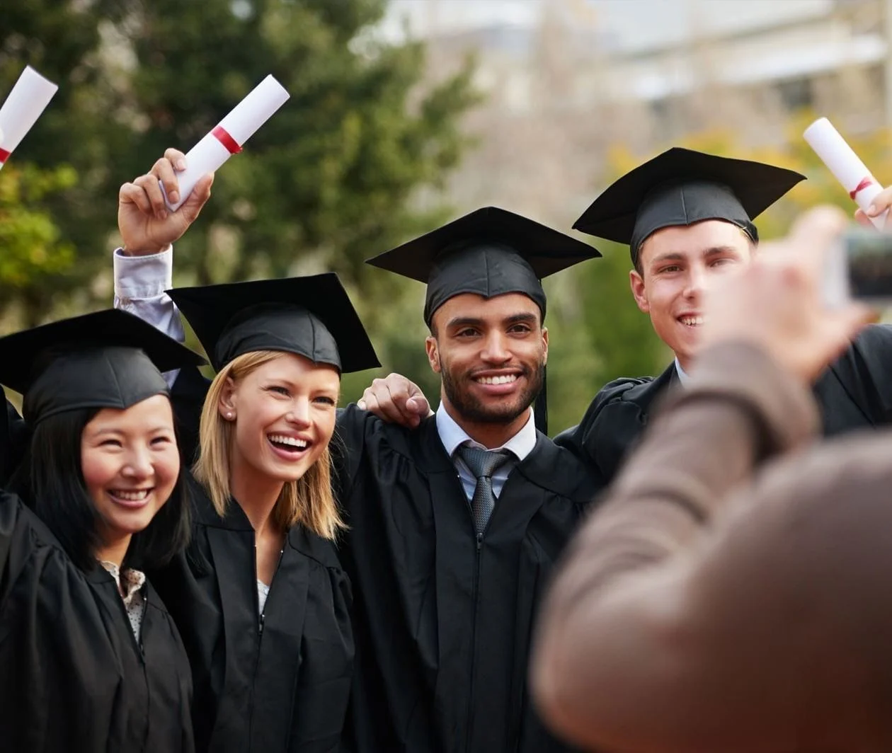 A small group of students celebrate graduating while a friend photographs their celebration