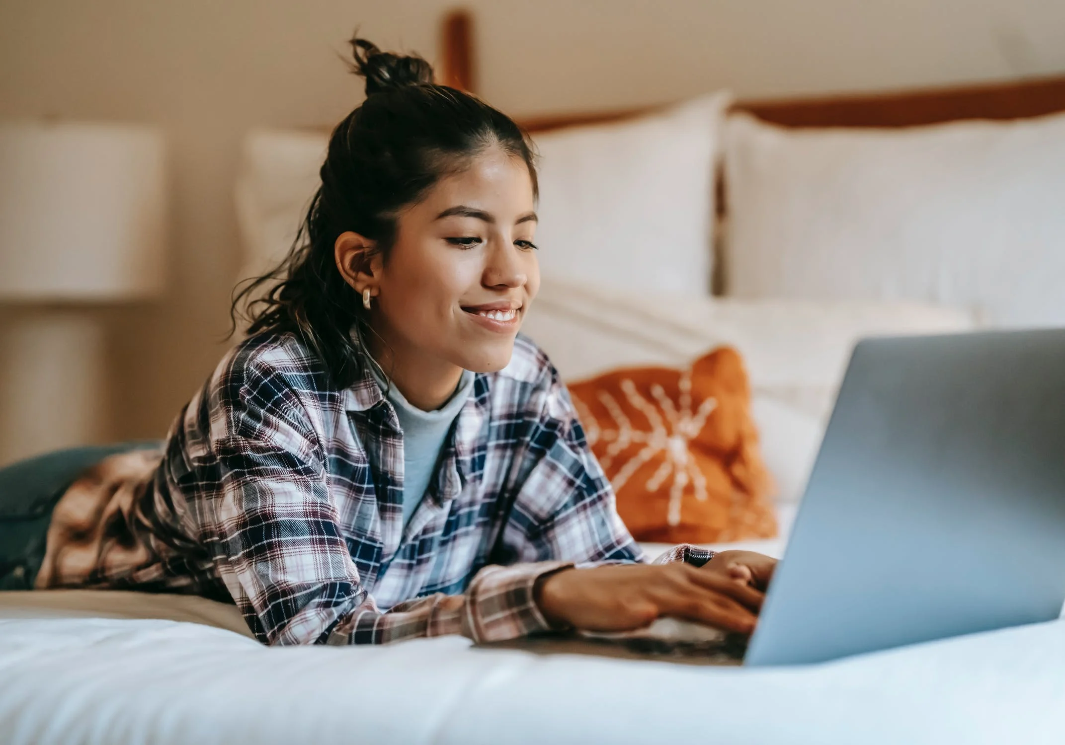 Woman smiling lying on bed typing on a laptop.