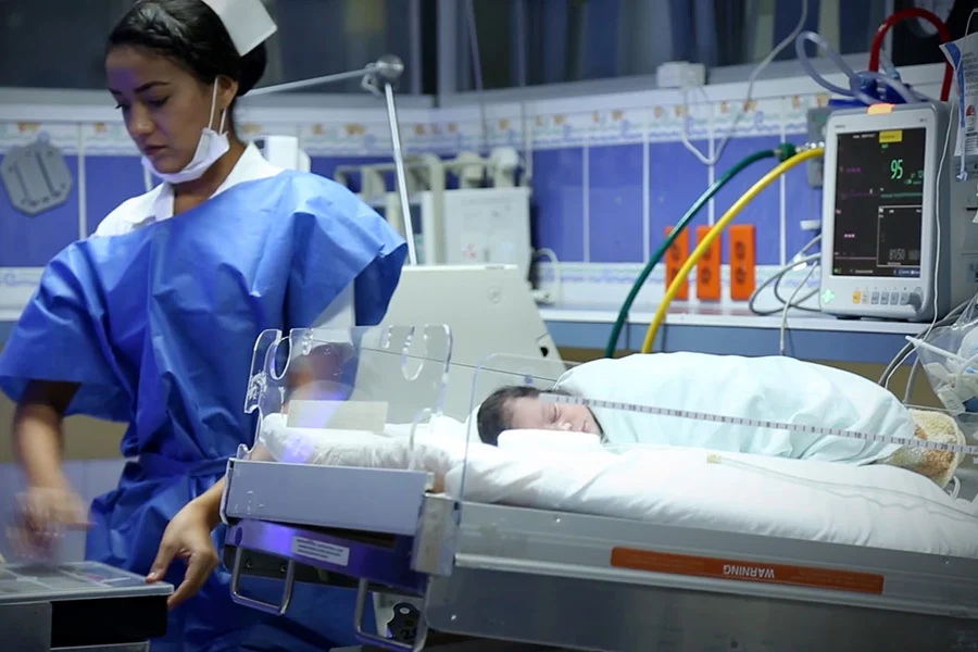 Nurse stands beside a sleeping baby in an open incubator