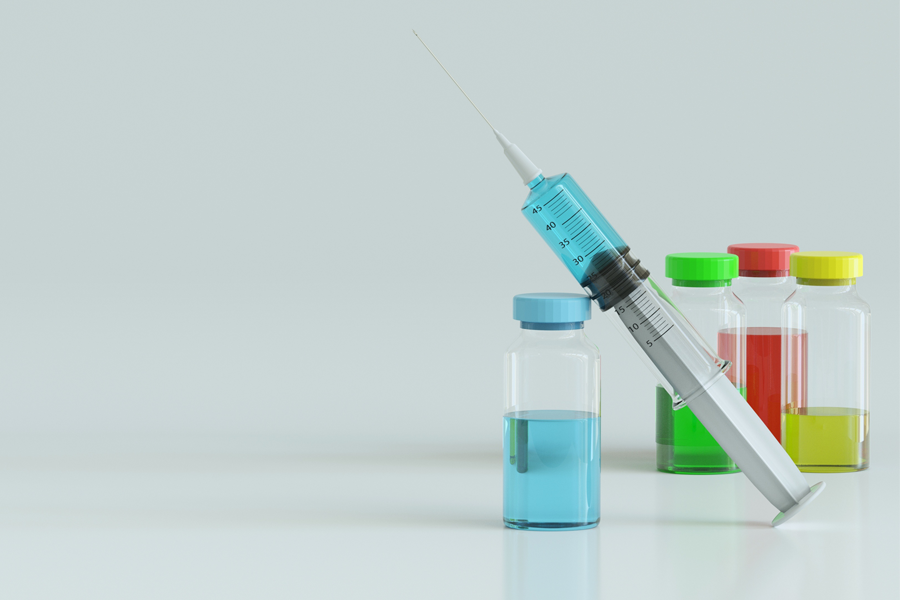 Four vials of coloured liquid with a syringe leaning against on one of the vials