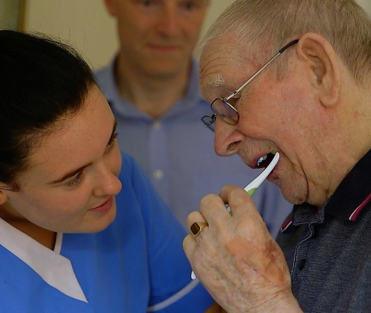 Carer helping clean an elderly man's teeth