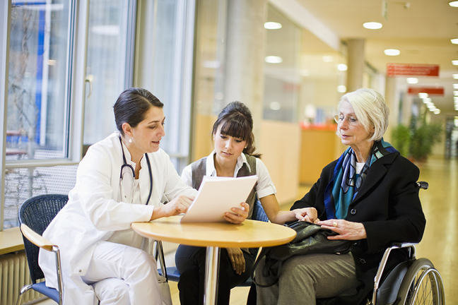 Female doctor discussing a care plan with an elderly female patient in a wheelchair and a younger woman