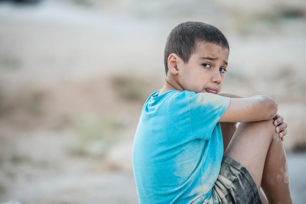 Young boy sitting on the ground with his hands around his knees