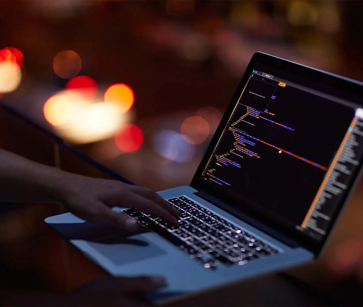 Person typing on laptop computer with coding lines displayed on the screen