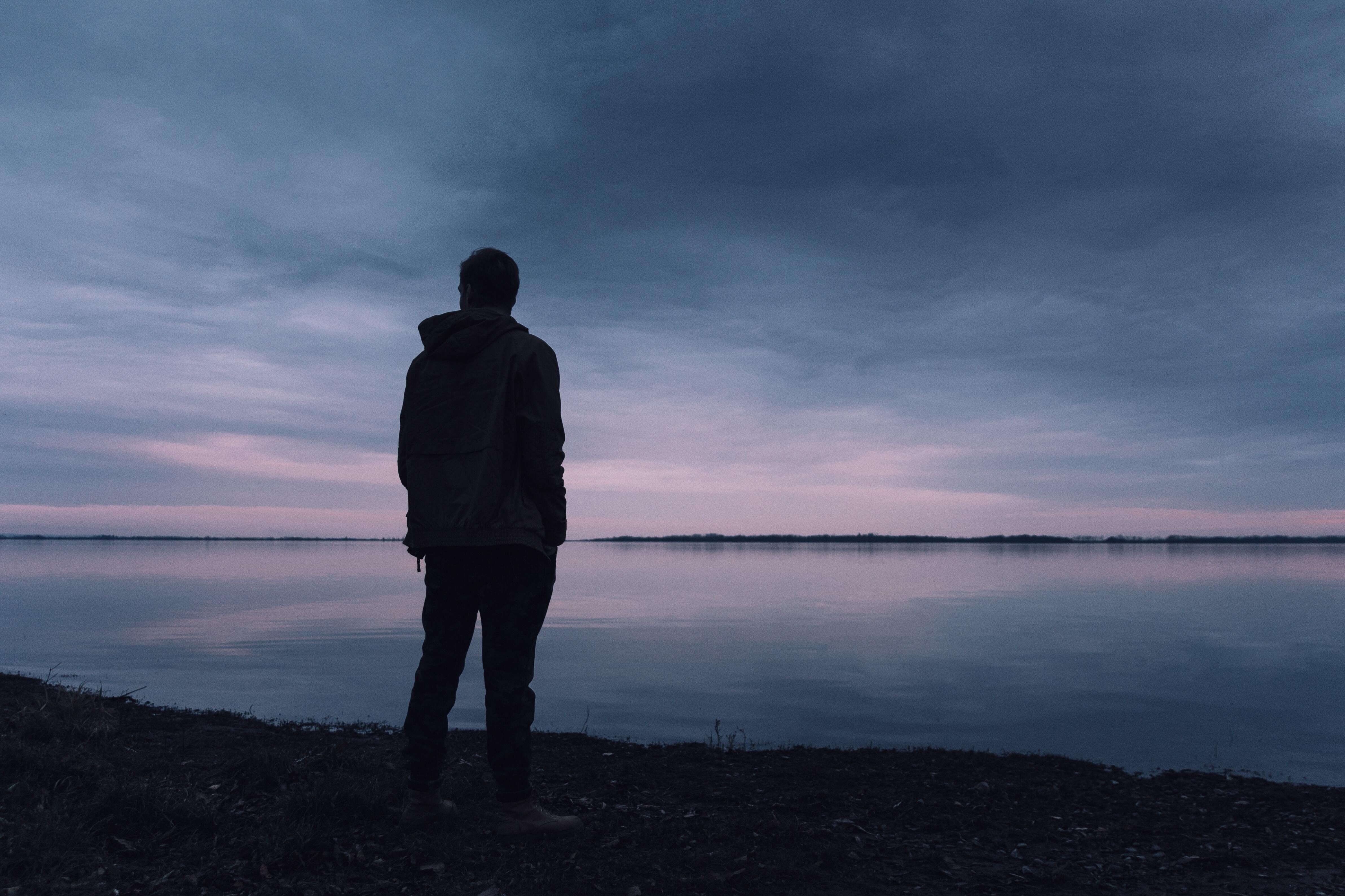 A man standing looking out at a lake.