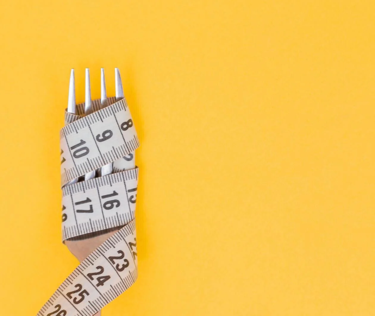 A measuring tape wrapped around a silver fork on a yellow background.