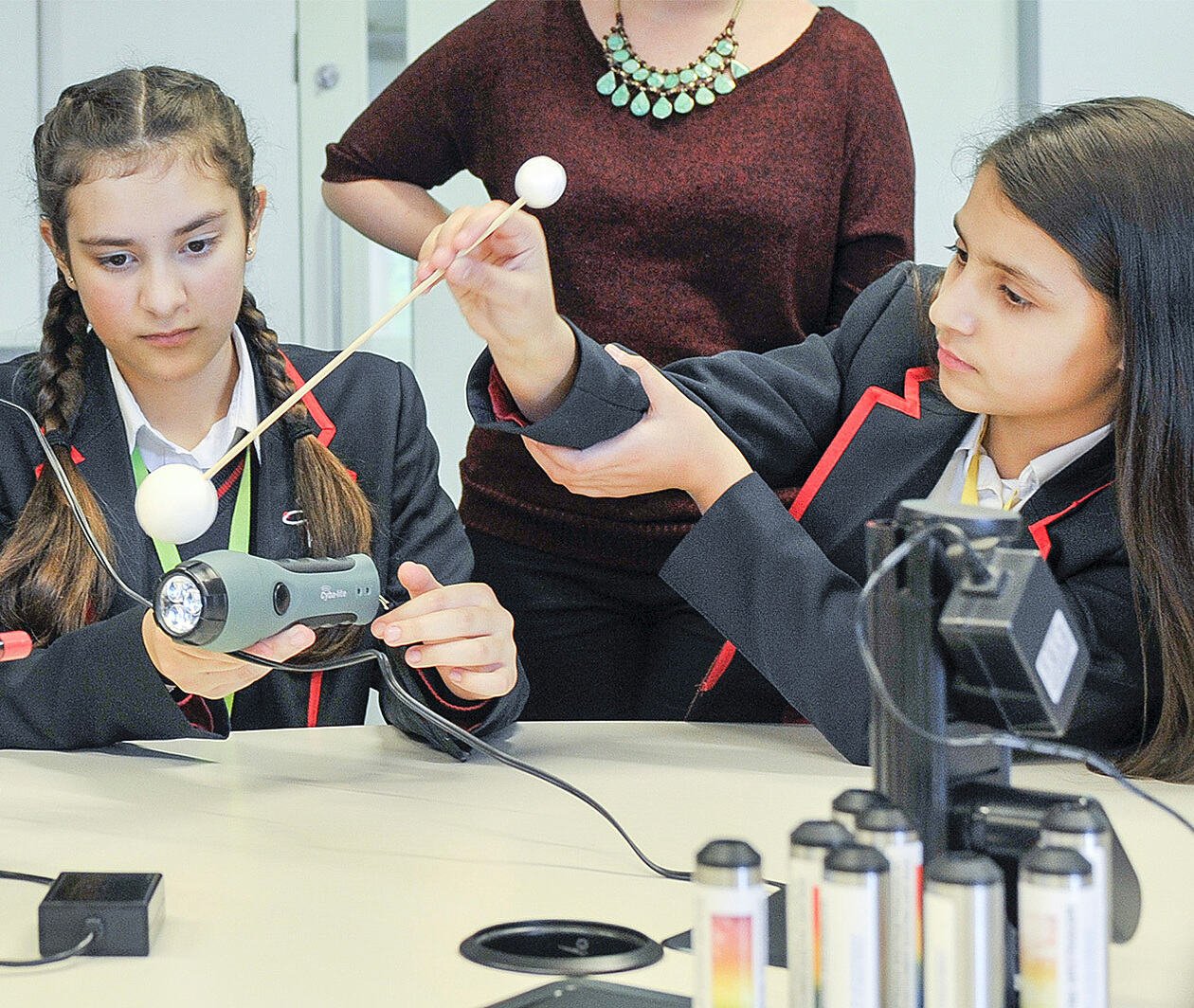 Teaching Secondary Science: young girls using science technology in a classroom as a teacher observes