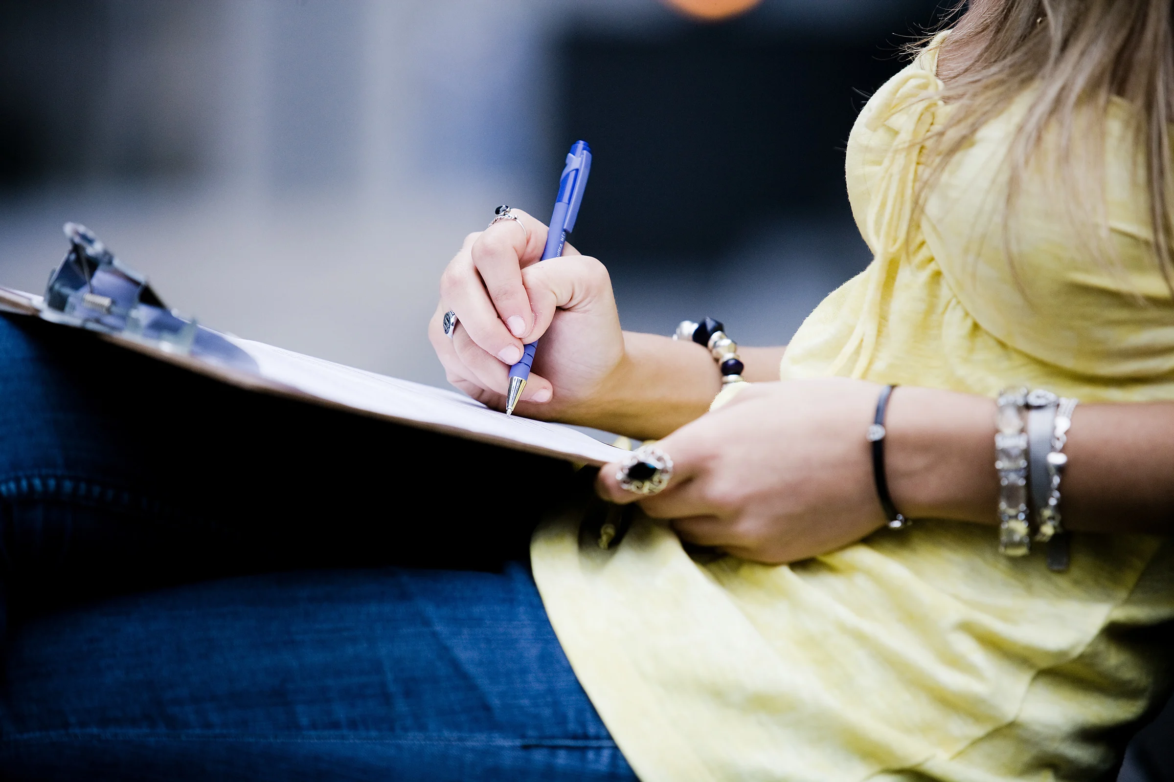 A woman sitting with a questionnaire in her hand filling it out with a pen.