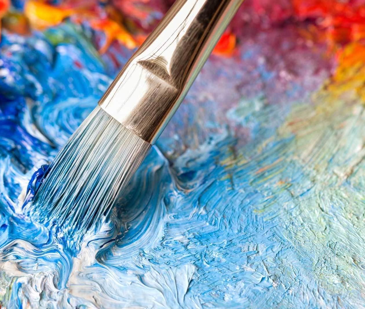 A painting brush mixing a colourful paint palette