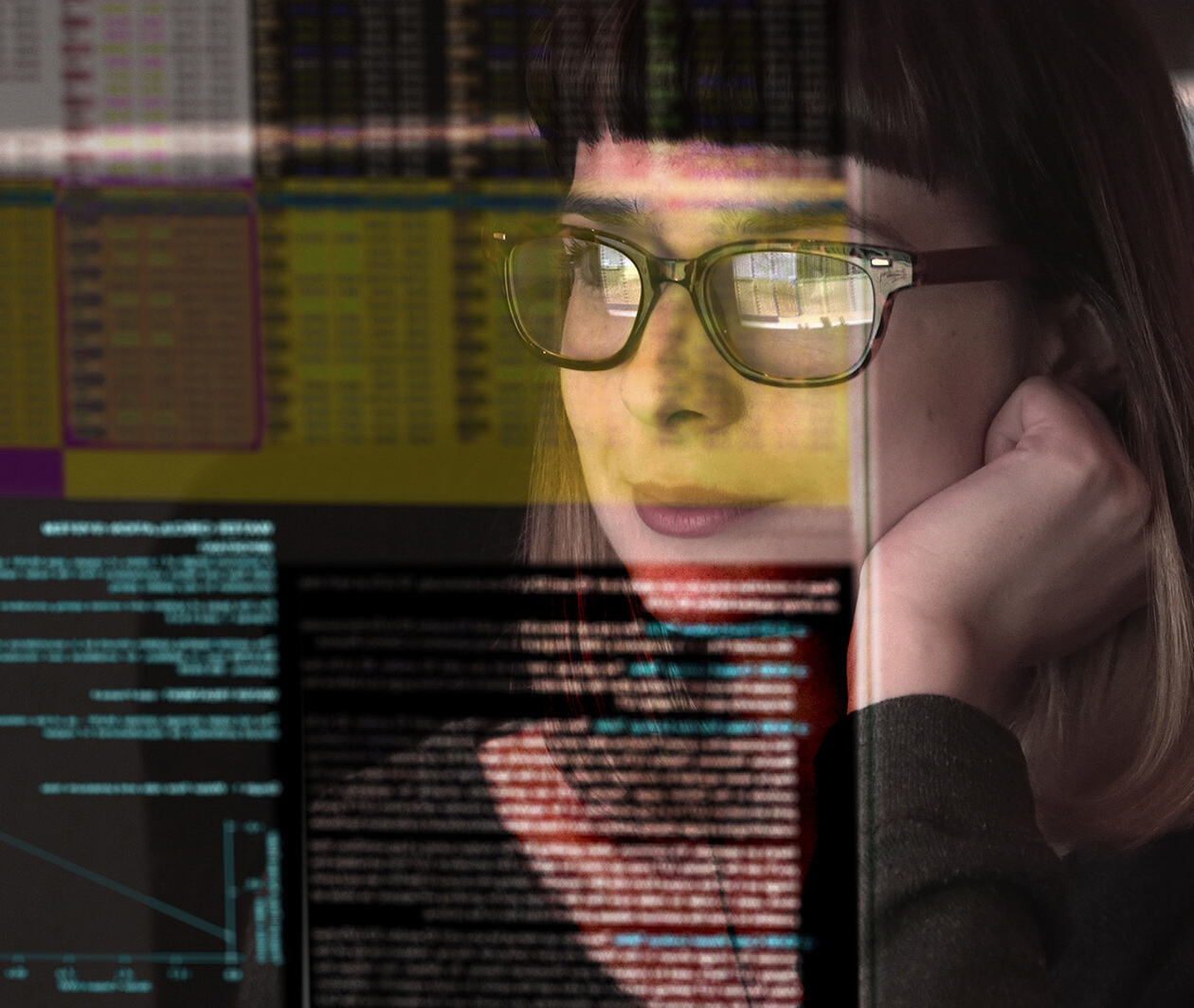 A woman with glasses observes data on a computer screen.