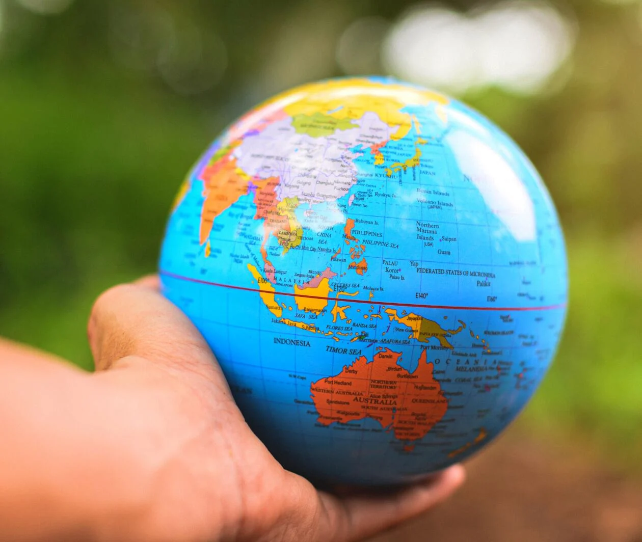 A closeup hand holding a small model of the globe focusing on Asia Pacific area