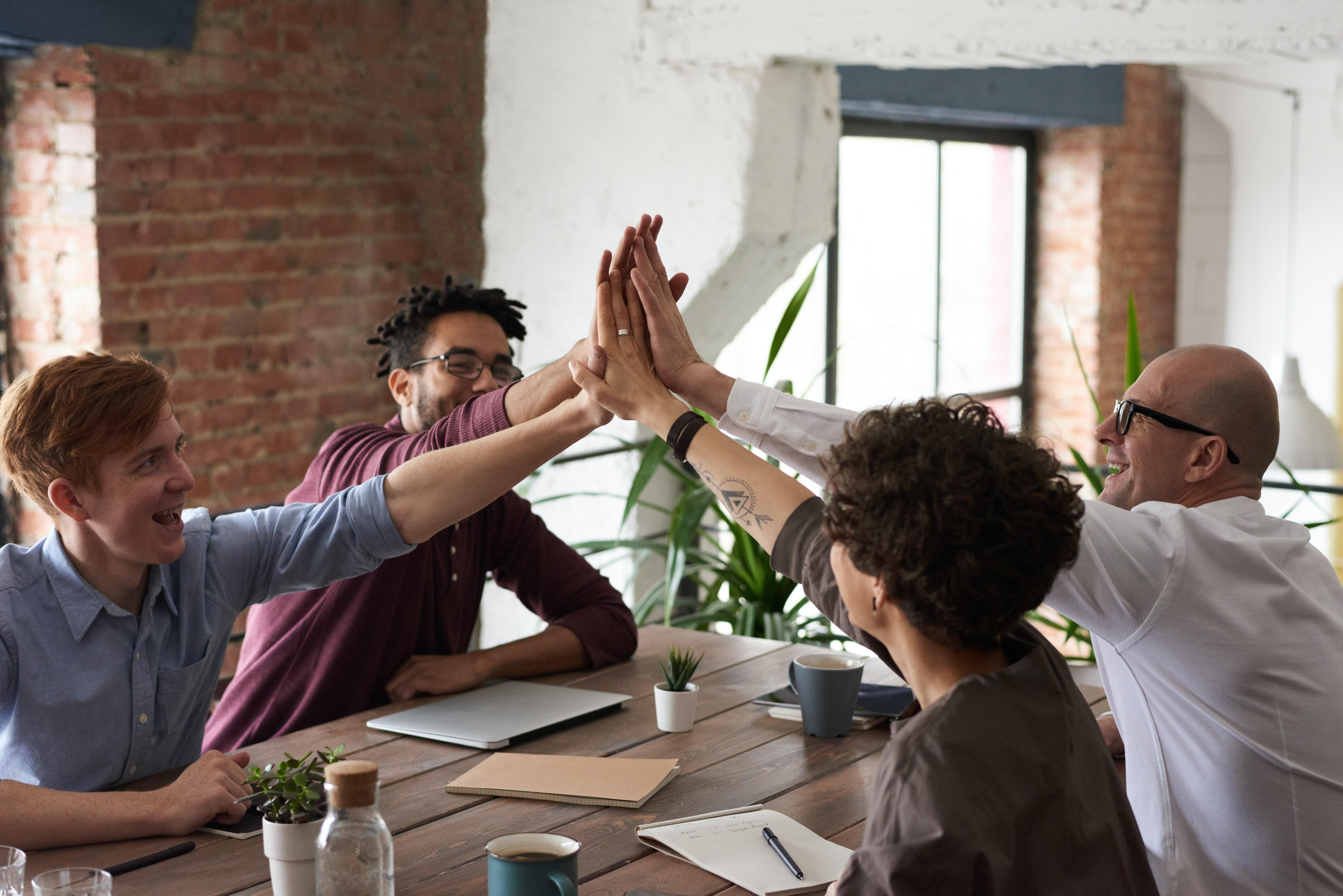 Four people sitting by a table, smiling and doing a high-five.