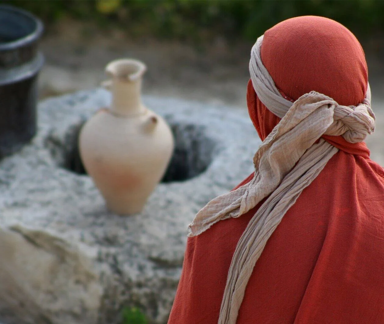 Robed person looking down at water well