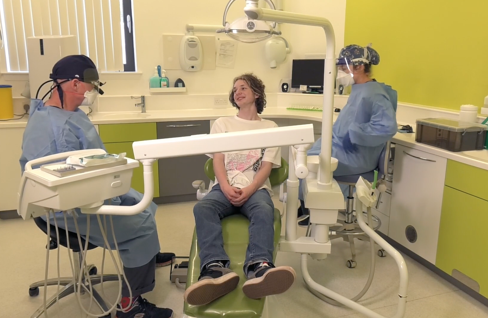 Two dentists wearing personal protective equipment speaking to a patient seated in a dental chair