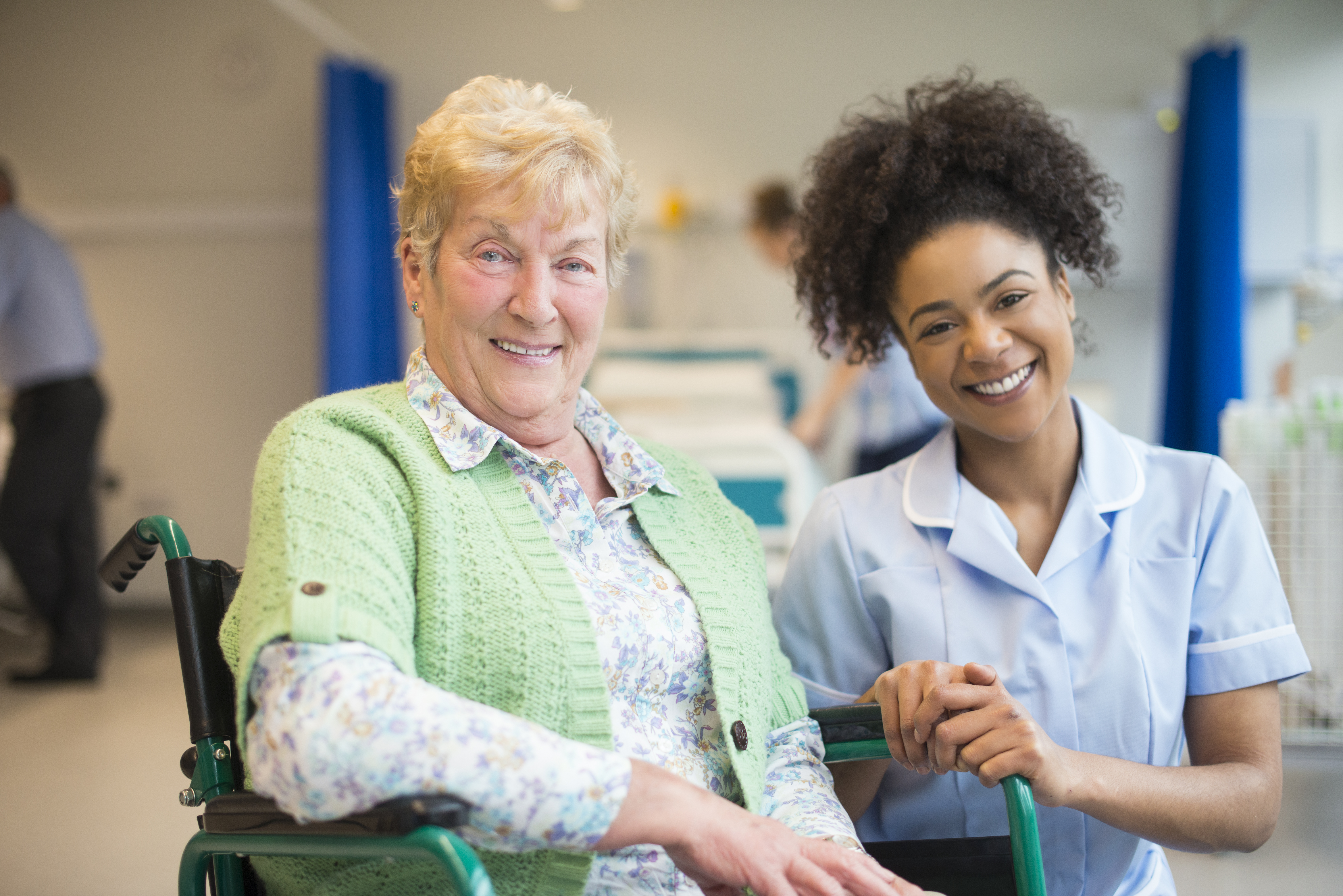 Senior female care home resident in wheelchair smiling alongside her female careworker