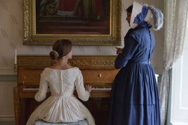 One person sitting by a piano and the other standing next to her.