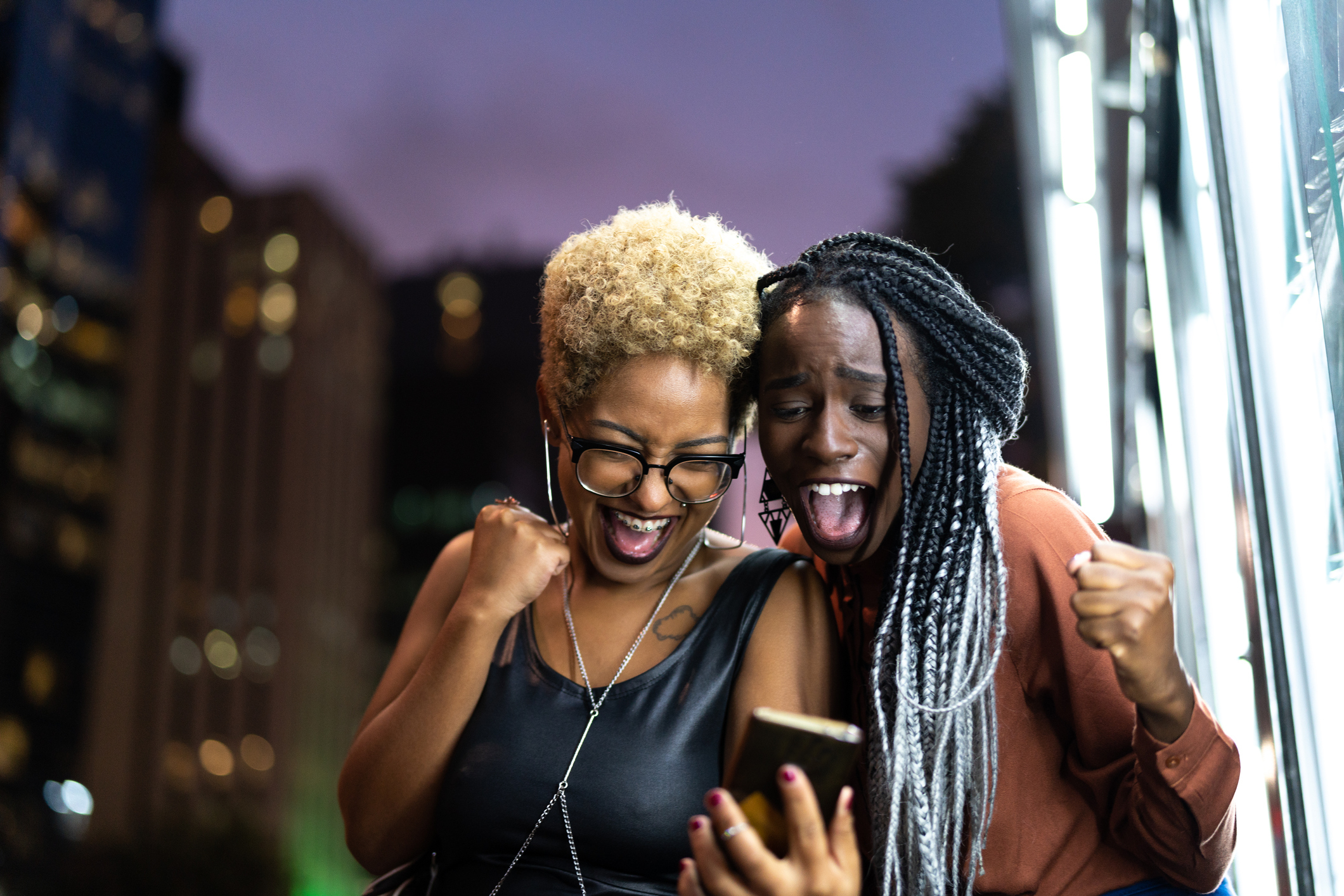 Two people looking at a smartphone and celebrating together.