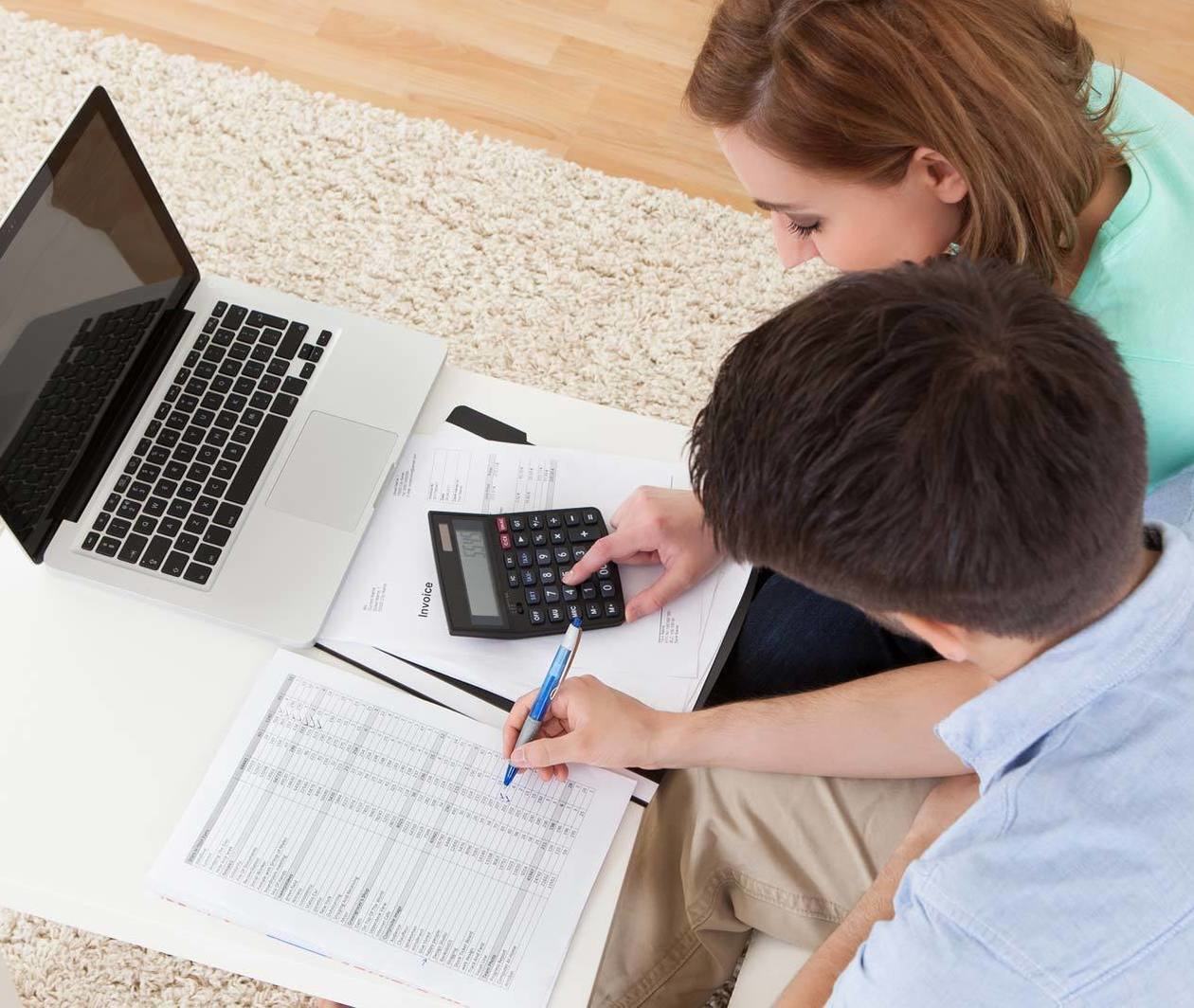 man and woman at desk with laptop, calculator and printed paper with table of numbers