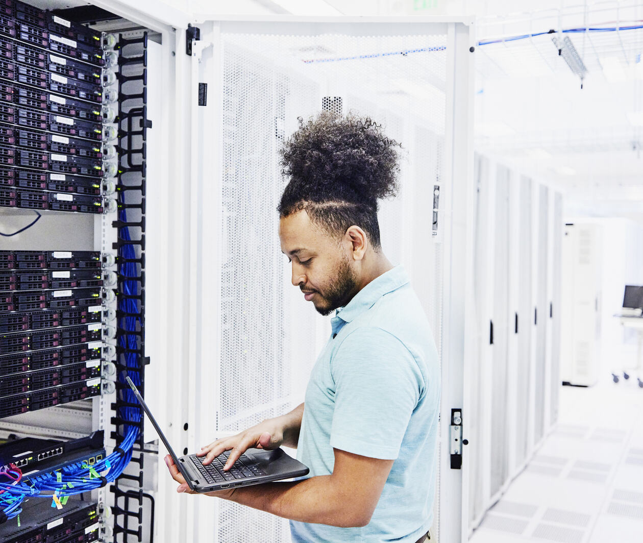 Man looking at a laptop while surrounded by servers.