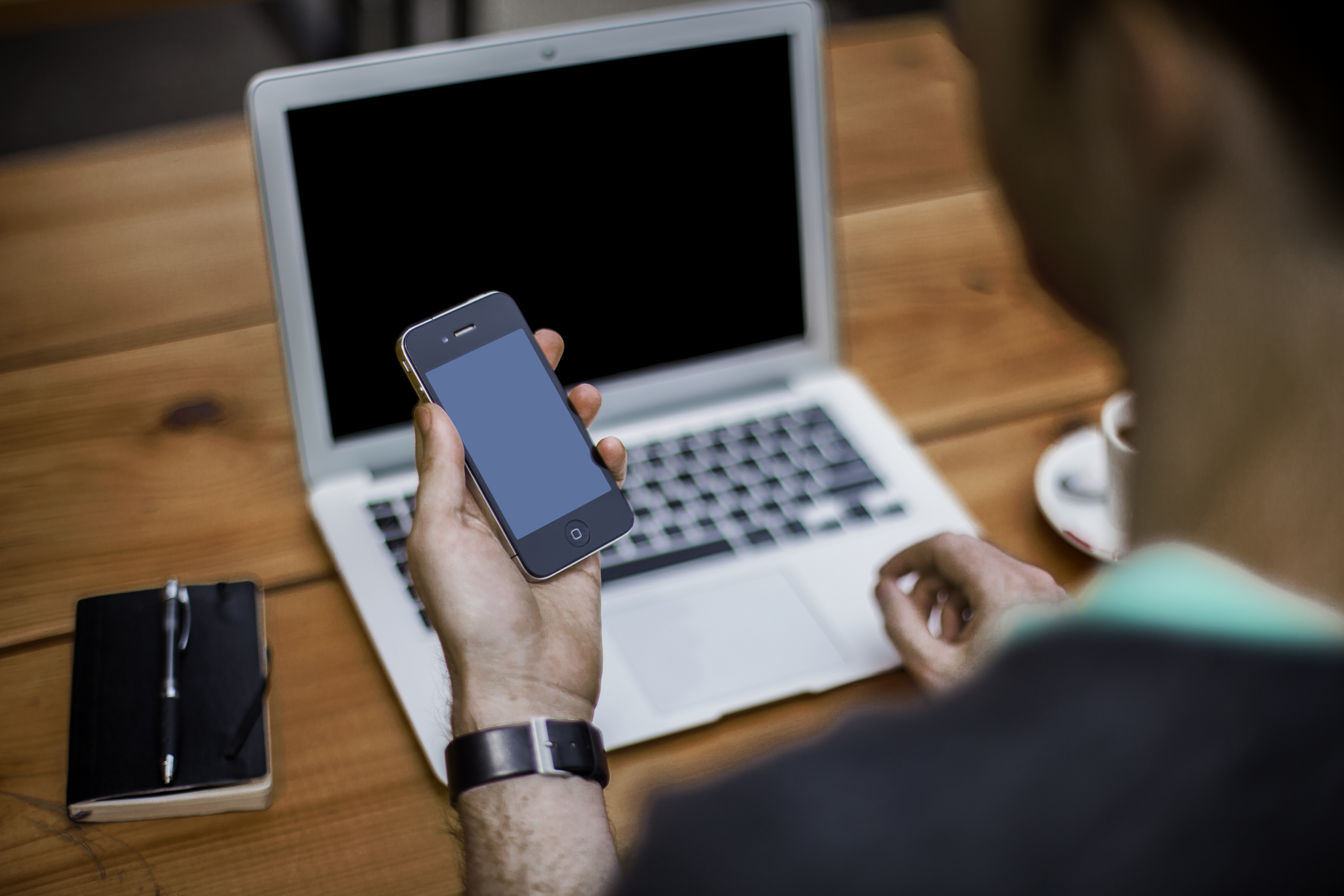 An image of someone sitting by a laptop holding a mobile phone.