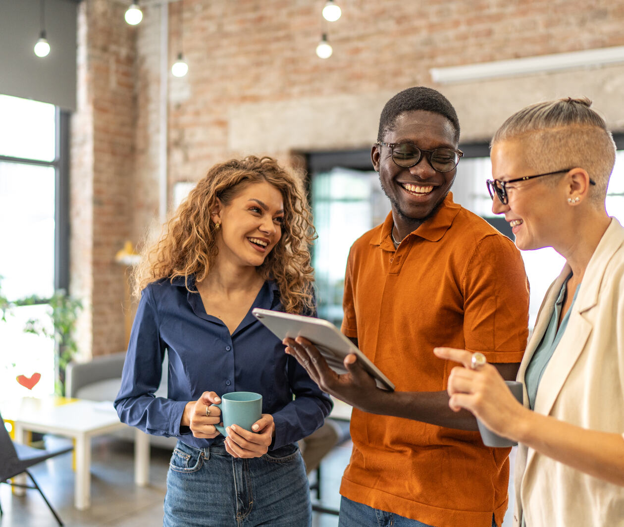 Diverse business professionals smiling and discussing work while looking at a digital tablet, fostering collaboration and teamwork in a creative, open-plan office environment