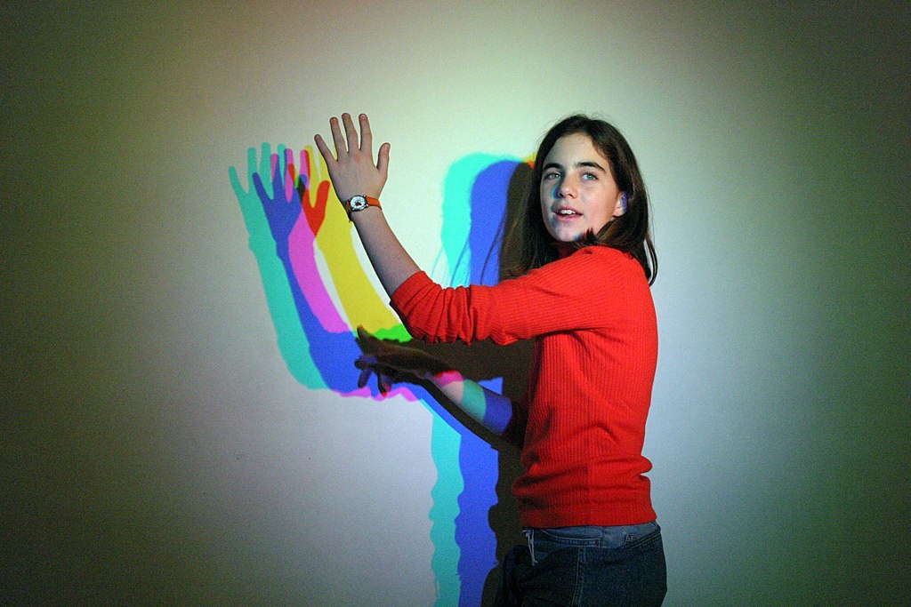 Woman stood in front of a white wall with a multicoloured shadow.