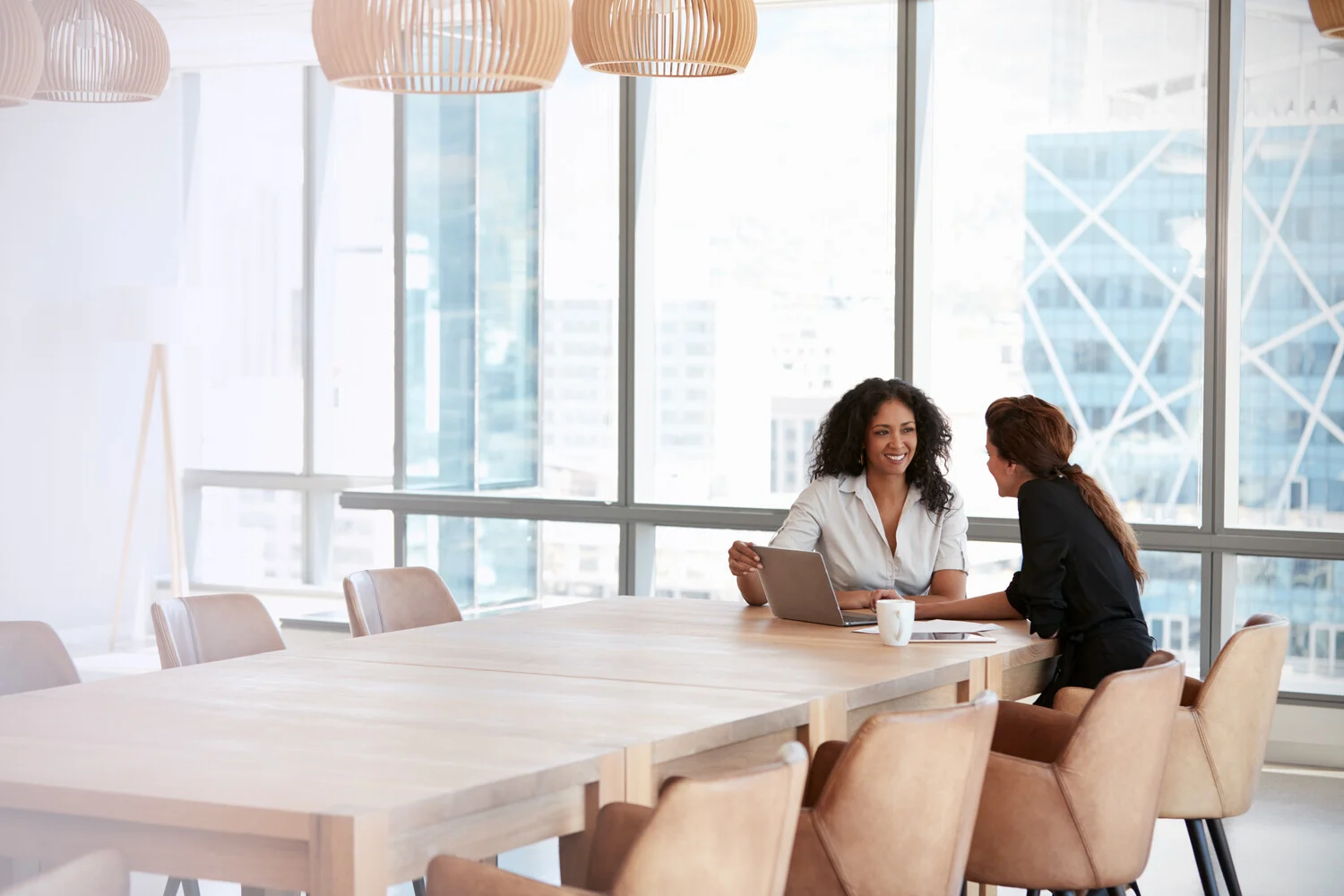 Image of two people talking at the end of a table sat with a laptop