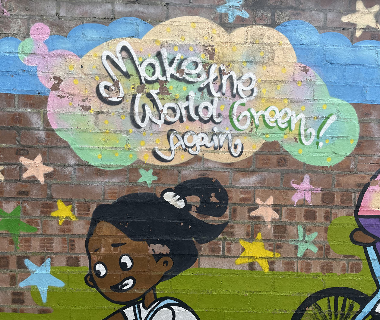 Street art of a young girl riding on a bike, with stars upon the sky and a big cloud with the message 'Make the World Green Again!', to represent sustainability and climate action.