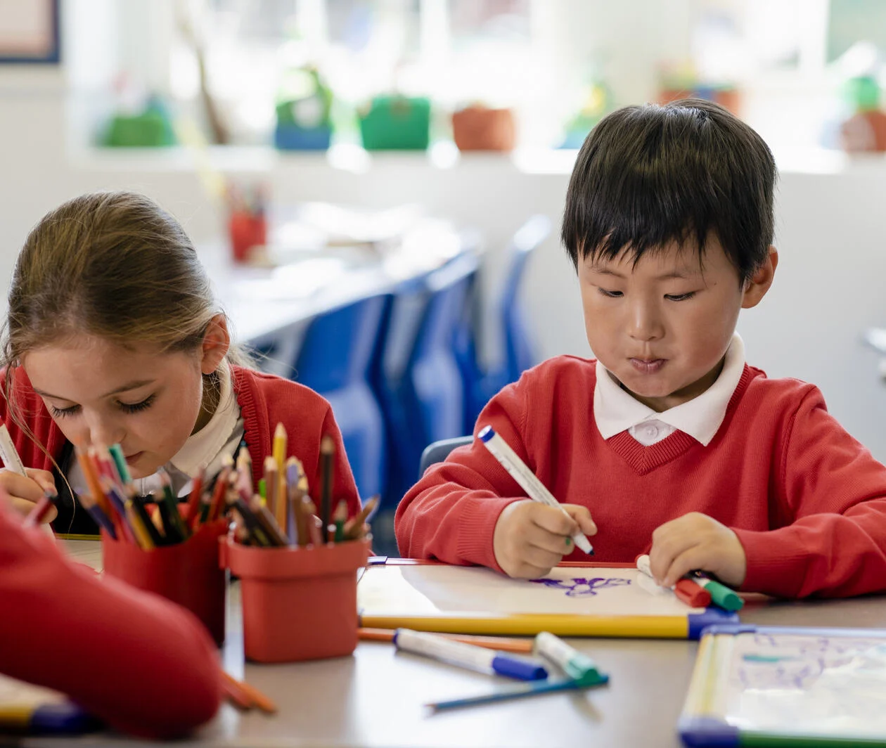 Two school pupils focusing on drawing with whiteboards.