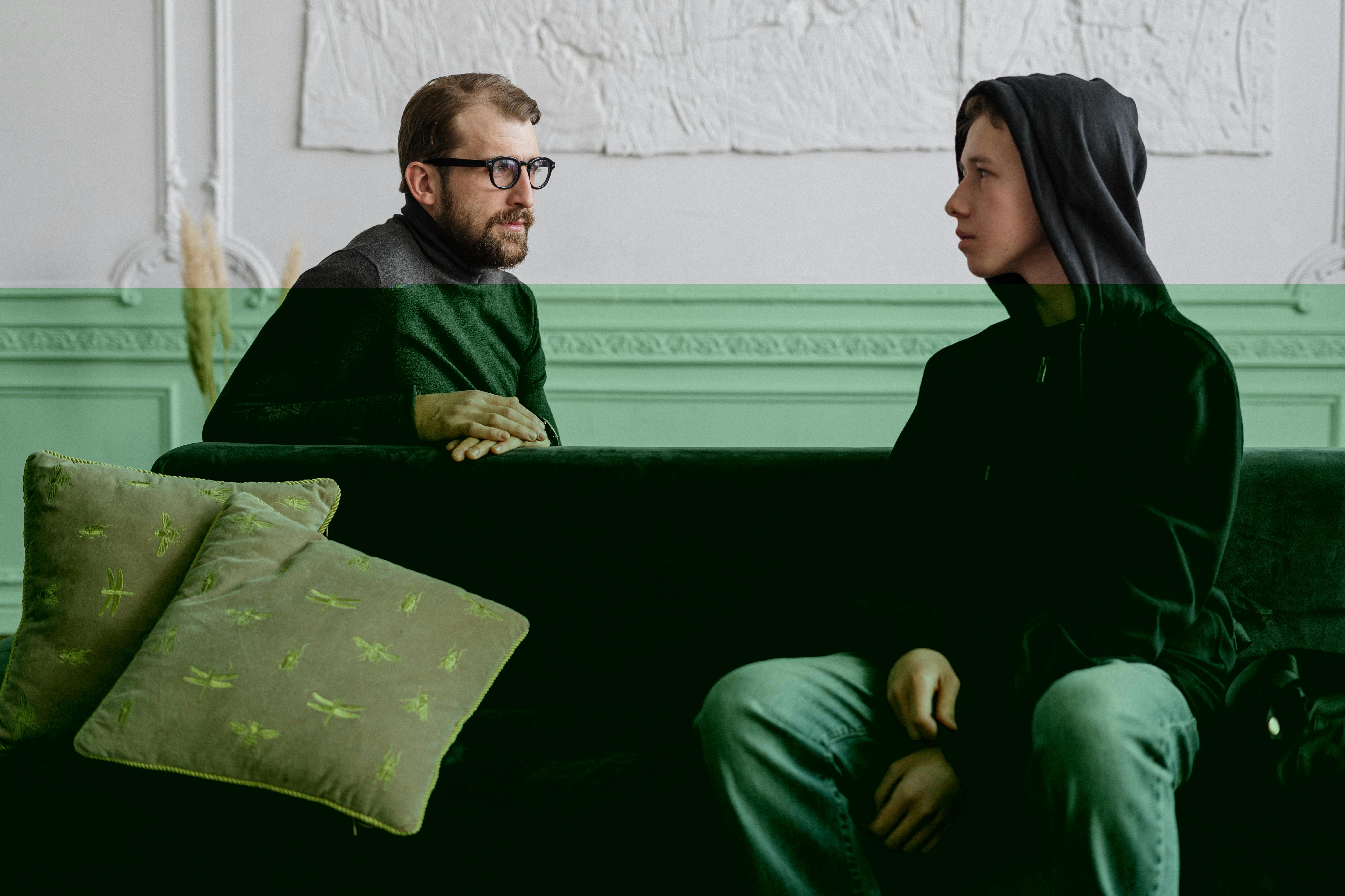 a man speaking to a teenage boy sitting on a couch