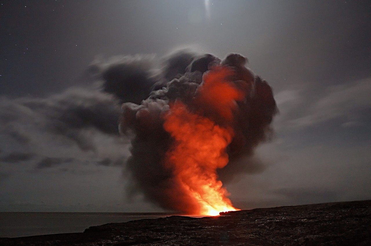 A volcano spouts hot ash into a darkened sky