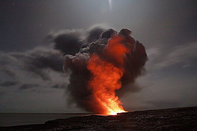 A volcano spouts hot ash into a darkened sky