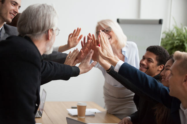 Group of diverse workers high five around a meeting table