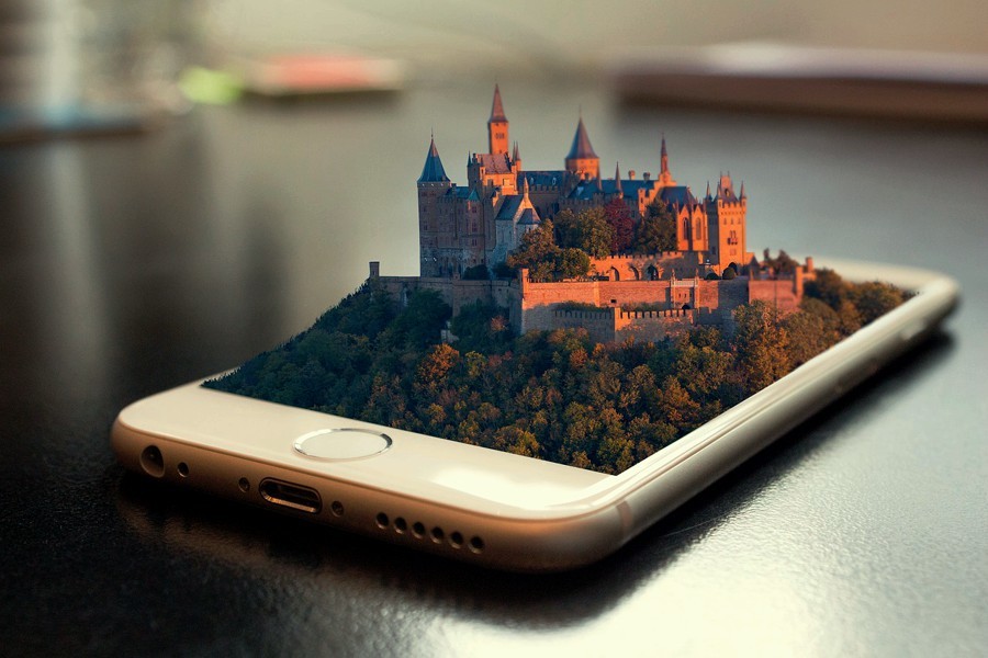 A large fortified building (perhaps a palace or monastery) emerges from the screen of a mobile phone.