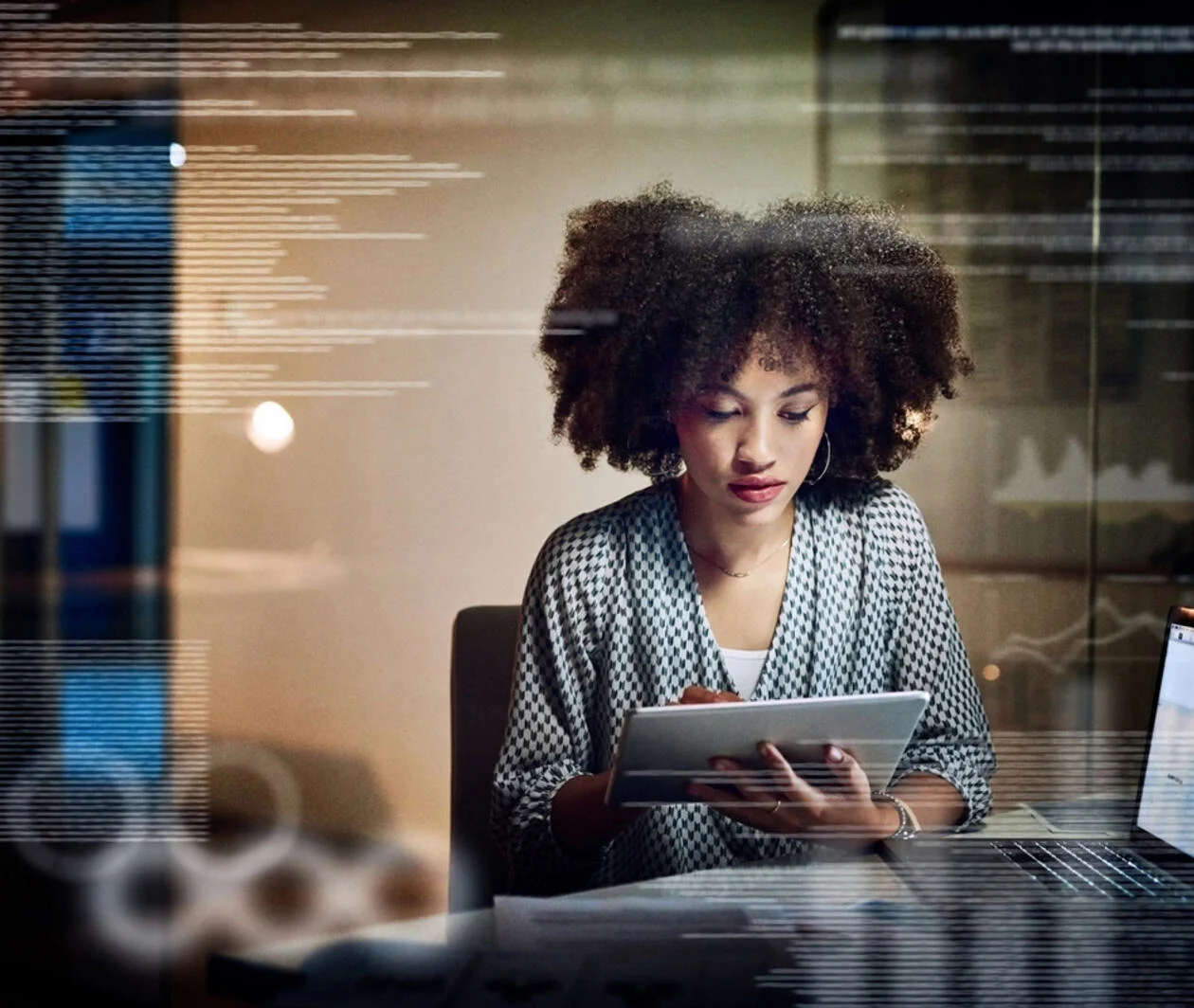 Women looking at a tablet. The is a glass screen in front of her that reflects graphs  