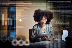 Women looking at a tablet. The is a glass screen in front of her that reflects graphs  