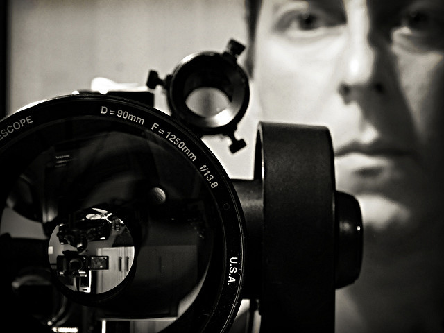 Black and white photo of man with a telescope lens in the foreground.