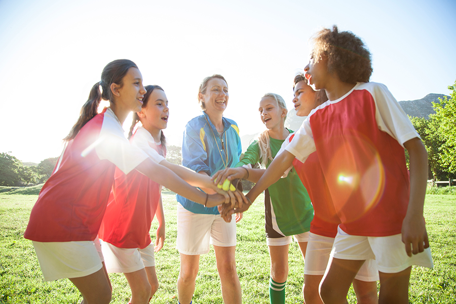 Girls’ soccer team (aged 12-13) doing a high five while preparing for a match