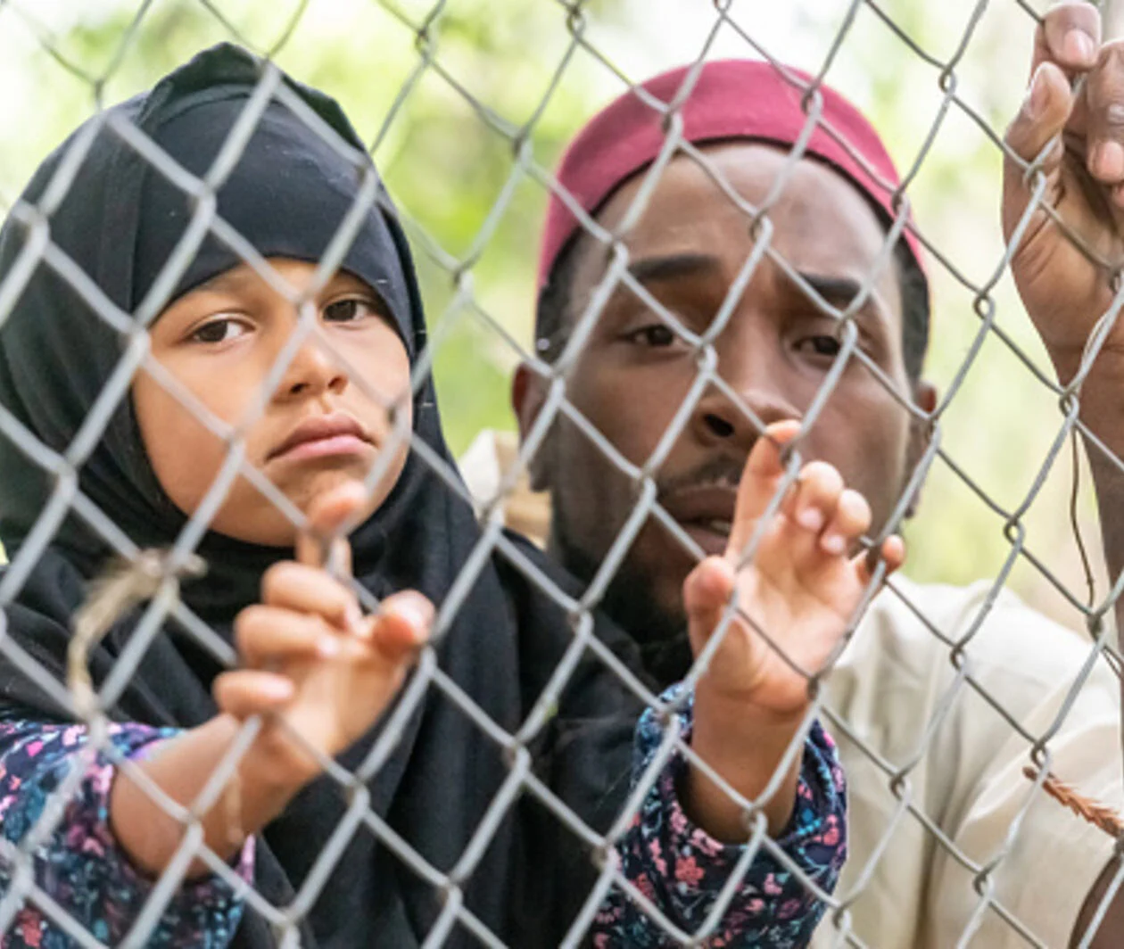 Muslim mid adult black man holding his daughter looking through a fence